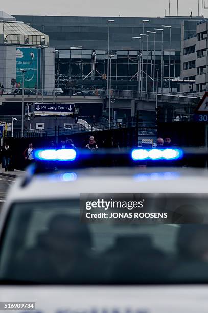 Picture taken on March 22, 2016 shows a Belgian police vehicle driving past passengers who are evacuating the Brussels Airport of Zaventem. At least...