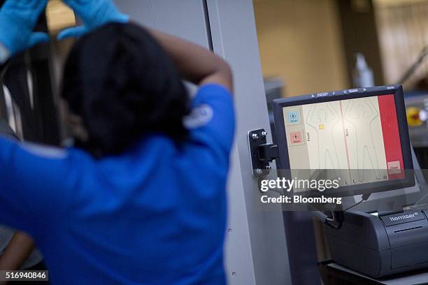 Transportation Security Administration officer, left, assists a passenger being screened by an automatic target detection machine in the TSA...