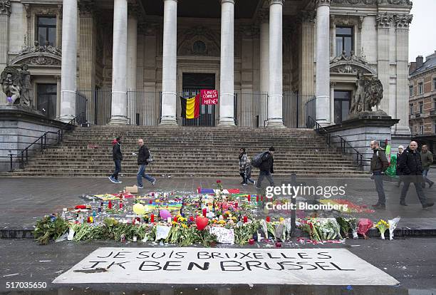 Pedestrians pass the Brussels stock exchange, operated by Euronext NV, as flowers and floral tributes sit on Beursplein square in Brussels, Belgium,...