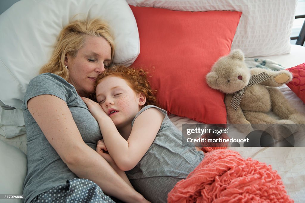 Mother and young daughter sleeping together in bedroom.