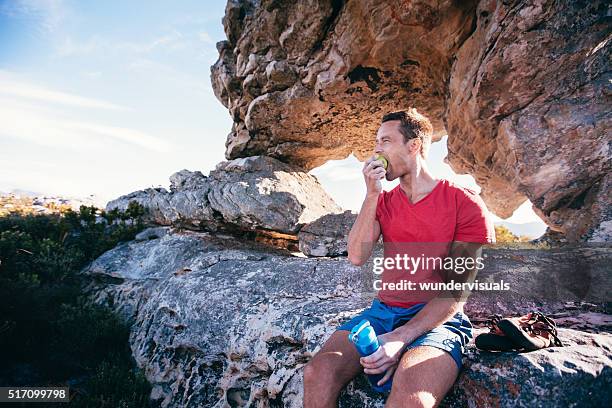 scalatore uomo mangia una mela per riposarvi dalle estreme di arrampicata su roccia - sportman foto e immagini stock