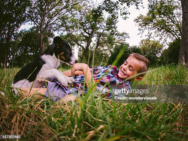 happy boy and his puppy dog frolicking around in grass - roll shirt stock pictures, royalty-free photos & images