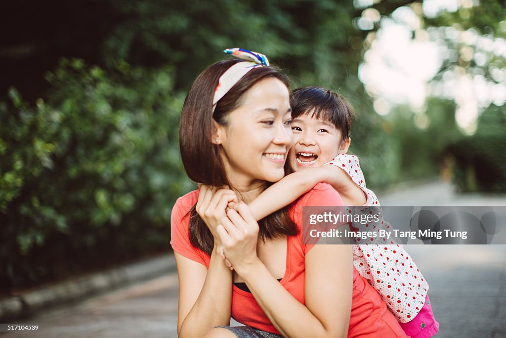 Toddler cuddling her mom from back in park