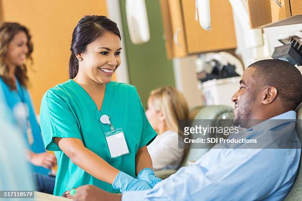 happy nurse comforting patient while he donates blood to hospital - blood transfusion stockfoto's en -beelden
