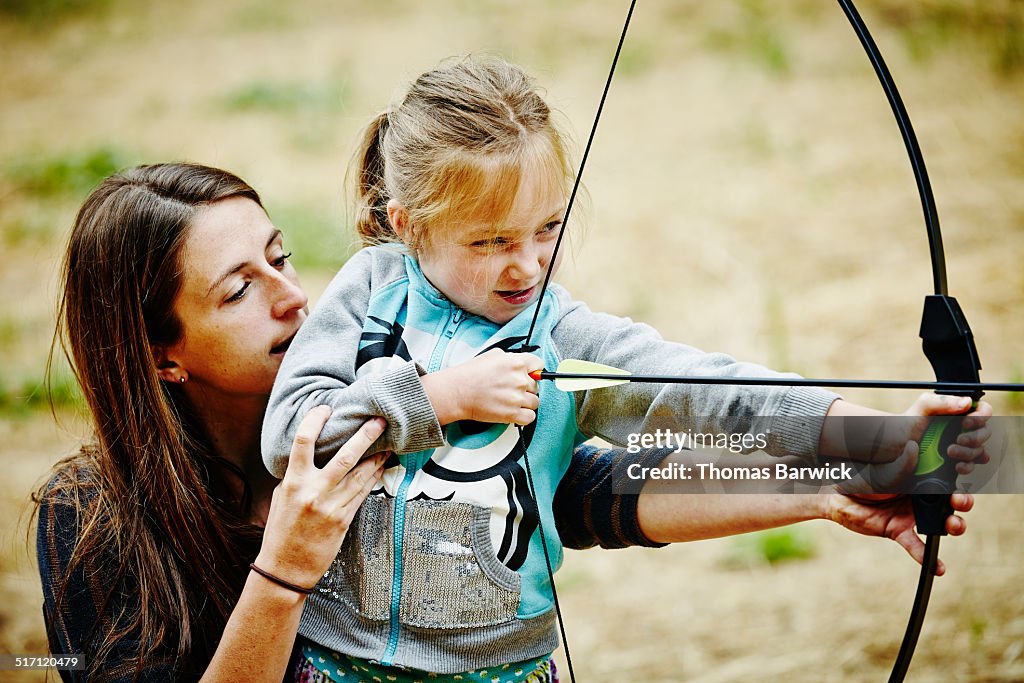 Camp counselor helping girl shoot bow and arrow