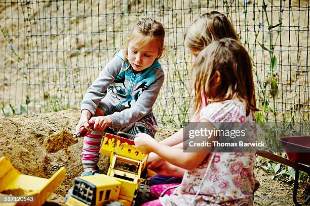 Three young girls playing with trucks in sandbox