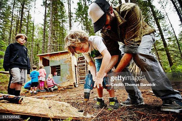 camp counselor helping young boy use drill - team building activity stockfoto's en -beelden
