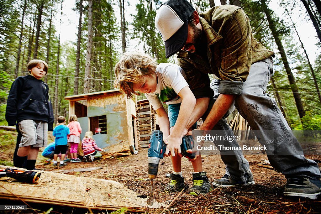 Camp counselor helping young boy use drill