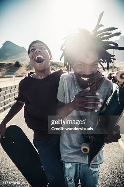 skateboarders laugh together, outside, with skateboards in hand - friends skating stock pictures, royalty-free photos & images