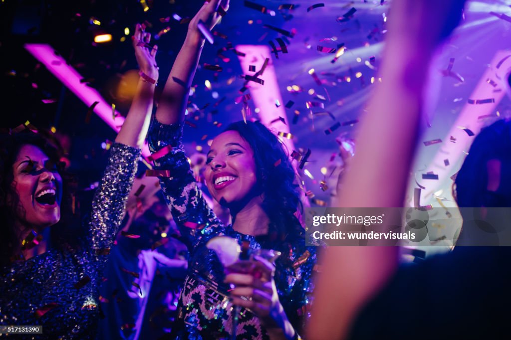Happy young friends partying with drinks and confetti in nightclub
