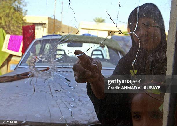 An Iraqi woman points 10 November 2004 to a bullet hole piercing a window pane opposite the house belonging to the cousin of Iraqi Prime Minister...