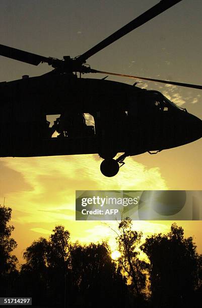 The sun sets, as a helicopter flies by as it leaves the outskirts of the restive city of Fallujah, 50 kms west of Baghdad 10 November 2004. Crouching...