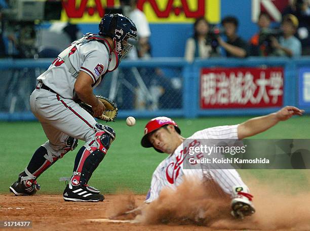 Hiroshima Carp infielder Shigenobu Shima slides home safely as catcher Johnny Estrada of the Atlanta Braves can't get the tag down in time during the...