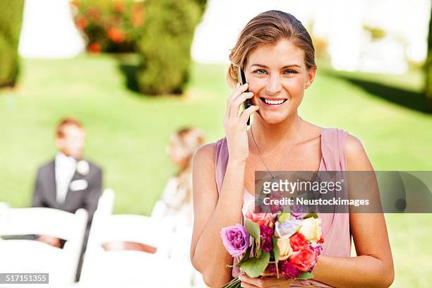 bridesmaid answering smart phone at garden wedding - familys revenge of the bridesmaids stockfoto's en -beelden
