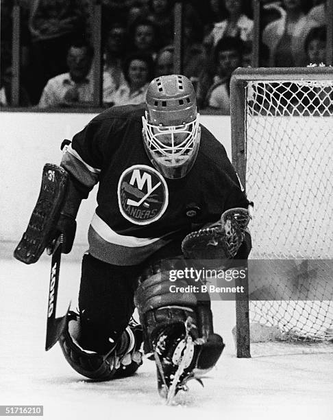 Canadian hockey player Billy Smith, goaltender for the New York Islanders, goes down on one knee and catches the puck during a game against the...