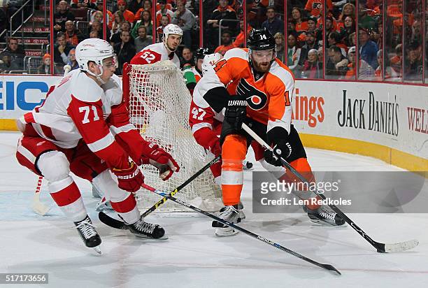 Sean Couturier of the Philadelphia Flyers skates the puck around the net against Dylan Larkin, Alexey Marchenko and Jonathan Ericsson of the Detroit...