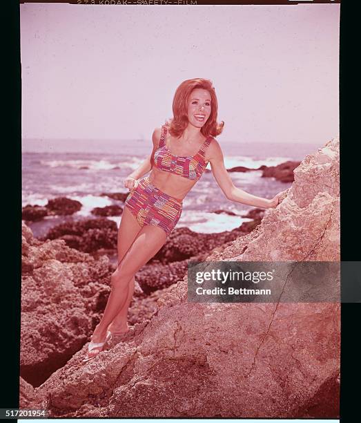 Actress Judy Carne posed in a bikini, leaning against the rocks. Photograph circa the late 1960s.