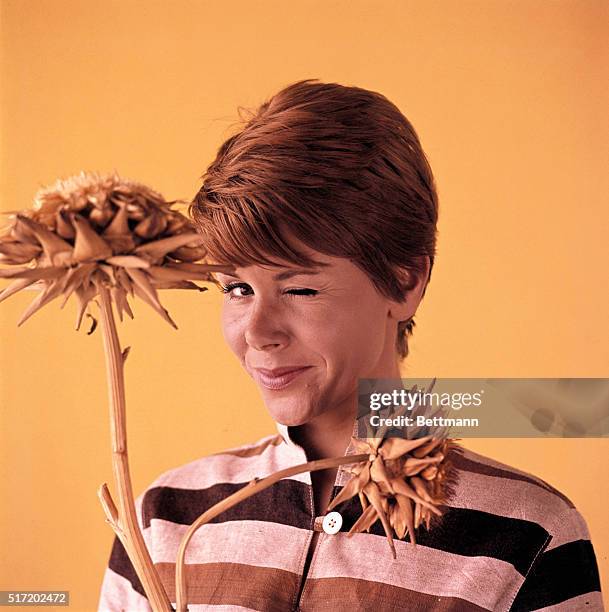 Comedienne Judy Carne, who starred in the television series Rowan and Martin's Laugh-In, shown here winking, holding a yellow dried flower.
