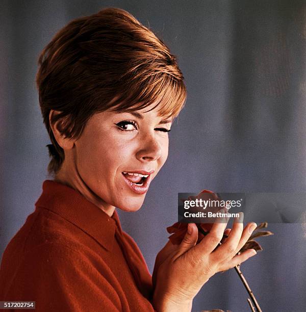 Comedienne Judy Carne, best known for her role in Rowan and Martin's Laugh-In, shown here winking and holding a red rose.