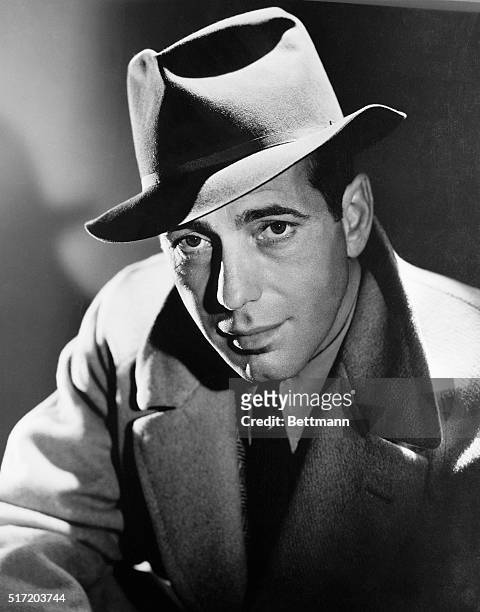 Actor Humphrey Bogart dons a fedora hat and overcoat.