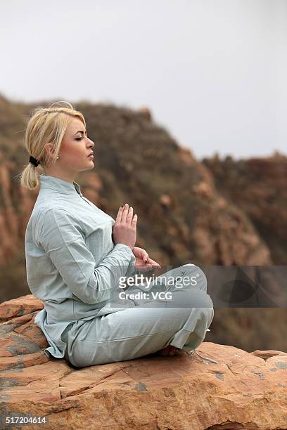 Foreign woman does yoga on the precipice of Mount Song on March 23, 2016 in Zhengzhou, Henan Province of China. Over 10 yoga enthusiasts practice on...