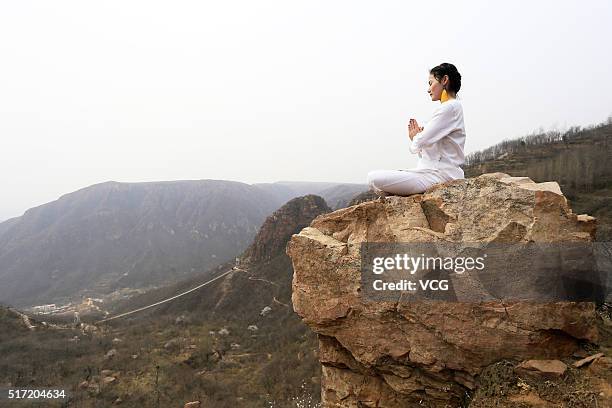 Woman does yoga on the precipice of Mount Song on March 23, 2016 in Zhengzhou, Henan Province of China. Over 10 yoga enthusiasts practice on the...