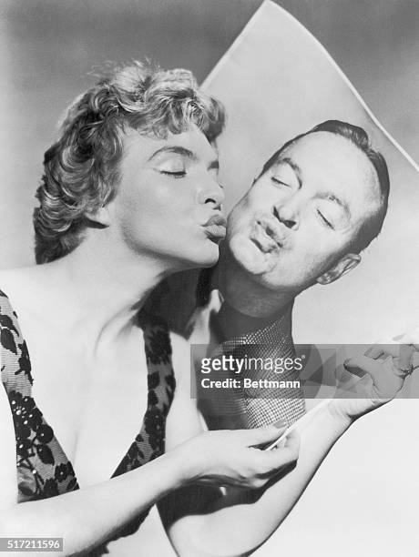 Line Renaud, French singing star who has just arrived in the U.S., gives a big kiss to a photo of comedian Bob Hope, who is returning the osculation...
