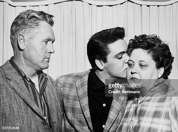 Singer Elvis Presley kisses his mother, Gladys, on the eve of his induction into the Army. At left is his father, Vernon.