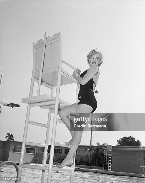 Portrait of Marilyn Monroe wearing a bathing suit posing by a lifeguard tower. Photo filed July 1, 1952.