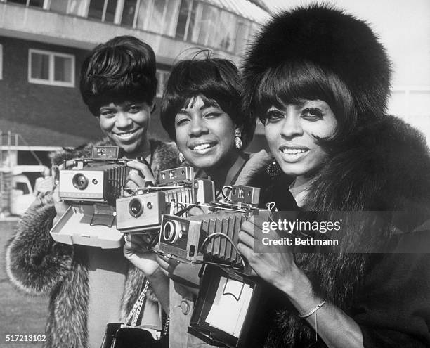 The Supremes pose with their cameras as they arrive at London Airport.