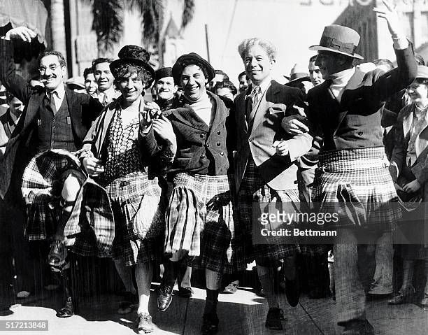 Publicity handout of the Marx Brothers and Sid Grauman wearing kilts. They are marching in some sort of parade. Undated photograph.