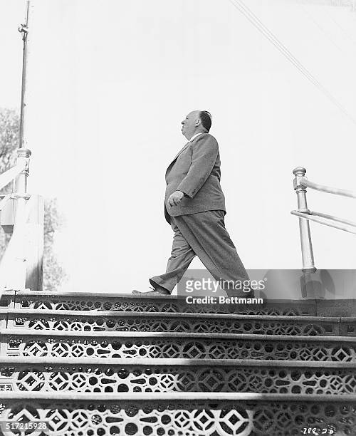 Photograph of famed English director Alfred Hitchcock walking atop steps.