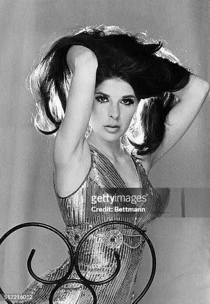 Photo shows singer Bobbie Gentry, wearing a glittering dress and running her hands through her hair in a seductress-type of pose.