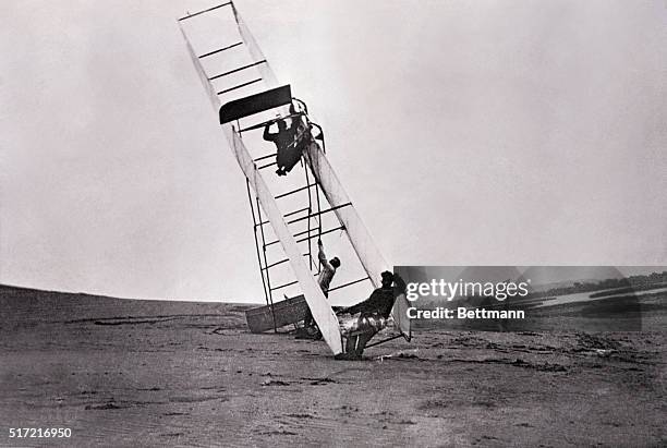 Orville Wright climbs out of a glider which made a less than perfect landing at Kitty Hawk in 1911. On the ground are Alec Ogilvie and Wilbur Wright.