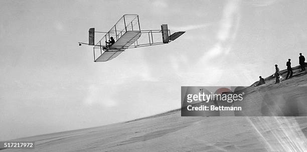 Orville Wright glides over Kitty Hawk in the Wrights' 1911 glider while others look on.