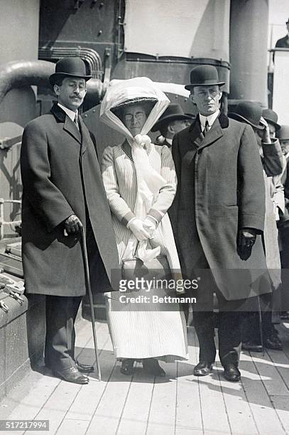 Full length portrait of inventors Orville Wright and Wilbur Wright standing with their sister Katherine Wright on the deck of a ship. Undated...