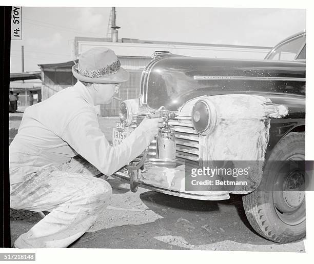 Workman is pictured spraying black paint on the headlight of an auto in order to make it efficient for night driving in case of a blackout. A soapy...
