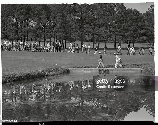 Golfing star Sam Snead is caught in the glass-smooth surface of a watering hole at the 15th green of the Augusta National Golf Course, as his caddy...