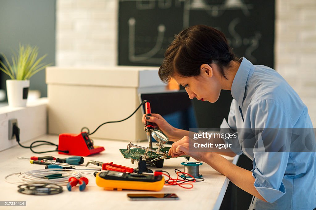 Woman Soldering a circuit board in her tech office.