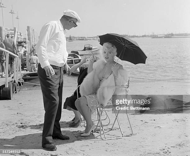 Marilyn Monroe, shading herself from the sun with an umbrella, talks to director Billy Wilder while both are on location in Coronado for Some Like It...