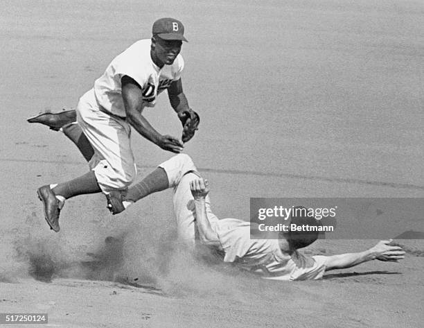 Jackie Robinson leaps into the air in an attempt to make a double play as Hank Sauer slides into second. The action took place during the second...