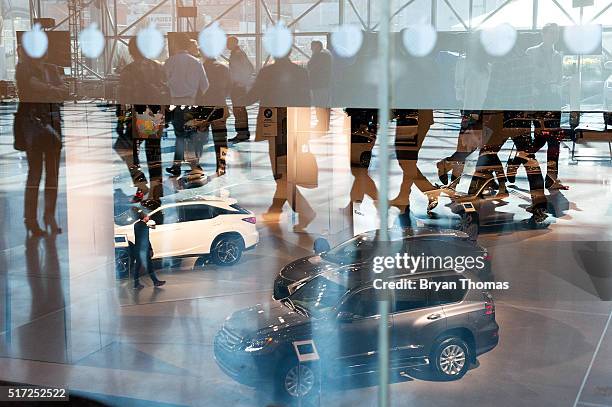 Members of the press are reflected in a window while visiting the New York International Auto Show at the Javits Center on March 24, 2016 in New York...