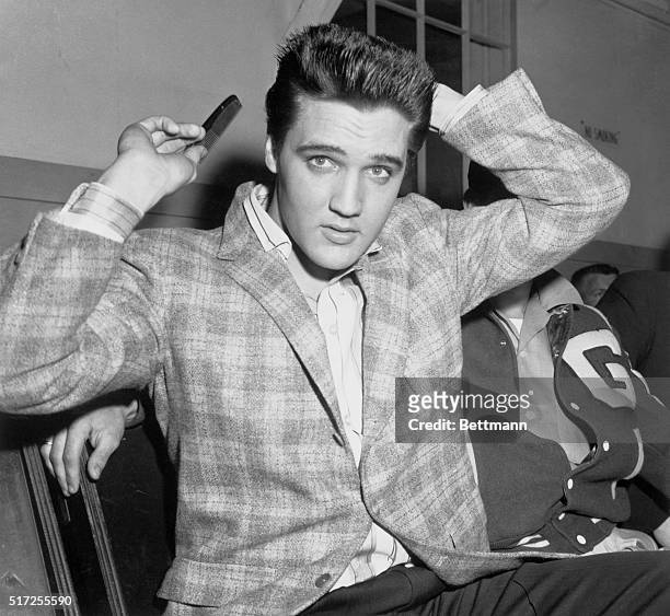 Elvis Presley runs a comb through his famous tresses at the Draftee Receiving Depot here on March 24th. The songster is scheduled for a trip to the...