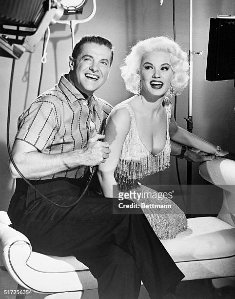 Playing the part of a Bachelor photographer, Bob Cummings seems to be enjoying himself as he prepares to snap the shutter on Mamie Van Doren. They...