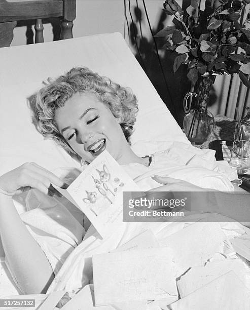 Shown here recovering from a recent operation for an appendectomy is glamorous motion picture actress, Marilyn Monroe as she reads a Get-well Card...