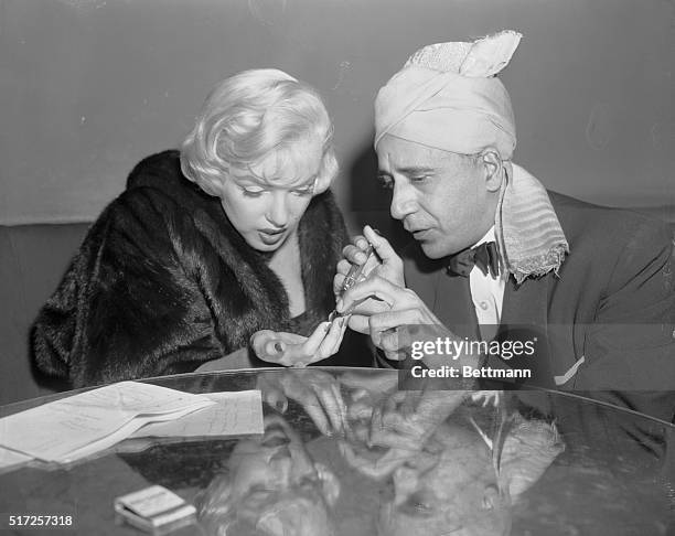 Marilyn Monroe has her palm read by Hassan, the fortune teller, at the Beverly Hills Hotel. The Swami said that the tell-tale lines indicated that...