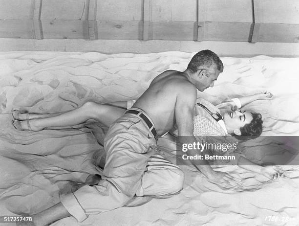 American actress Joan Crawford and Jeff Chandler act out a scene from the movie Female on the Beach while lying on the sand together.