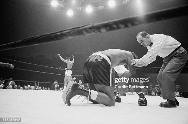 Victorious Cassius Clay waves his arms in background after knocking out Charlie Powell, being counted out by referee Ernie Sesto, in the third round...