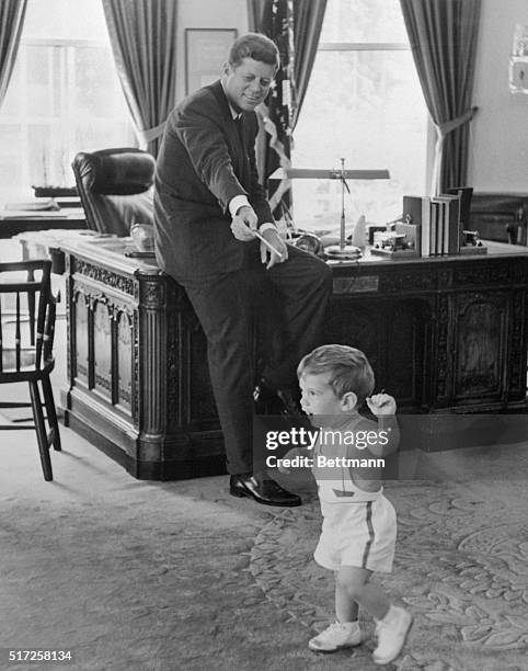 The White House released this picture showing President Kennedy watching his 18-month-old son, John Jr., prancing about in the Chief Executive's...