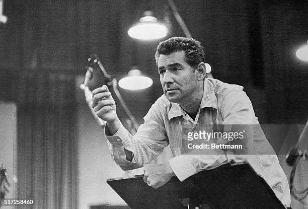 Waist-up portrait of Leonard Bernstein, conductor, with hand raised.